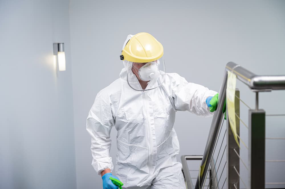 A Green Clean Team staff member in full PPE carefully disinfecting a staircase banister during a professional biohazard clean in Bendigo, Central Victoria.