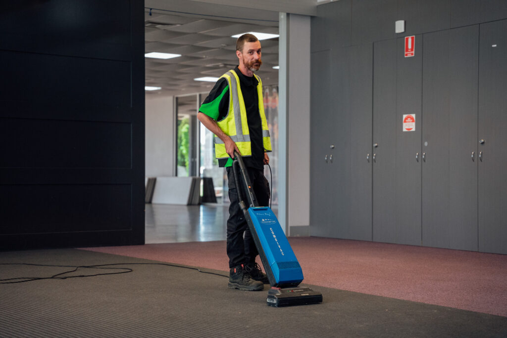 A Green Clean Team employee vacuuming a floor in a large industrial space